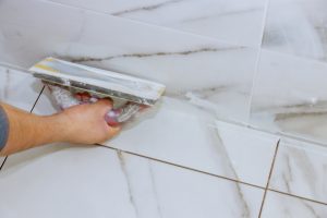 Bathroom tiling by manual worker grouting tiles with trowel cement mortar